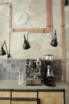 a coffee machine sitting on top of a counter next to a wall mounted clock with copper piping