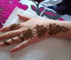 a woman's hand with henna tattoos and rings on her fingers, sitting on top of a bed