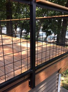 a wooden deck with black iron fencing around it and some trees in the back ground