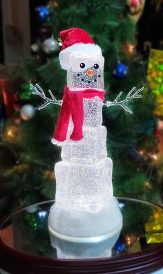 a snowman made out of ice on top of a glass table next to a christmas tree