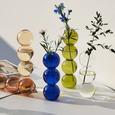 three different colored vases with flowers in them on a table next to a magazine