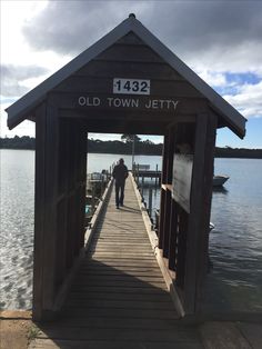 a man walking across a wooden pier towards the water with a boat in the background