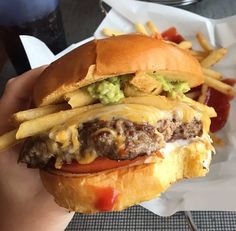 a hand holding a cheeseburger with fries and ketchup on the side