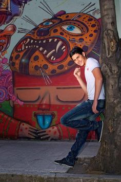 a man leaning against a tree in front of a mural