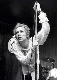 a young man holding onto a microphone while standing in front of a drum set