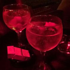 two wine glasses sitting next to each other on top of a table with pink liquid in them