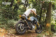 a man riding on the back of a motorcycle down a dirt road in the woods