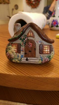 a ceramic house sitting on top of a table next to a roll of toilet paper