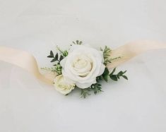 a white rose and greenery corsage on a white background with an ivory ribbon