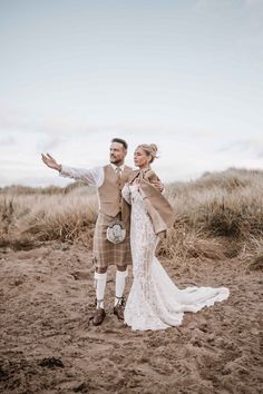 a man and woman standing in the sand with their arms spread out to each other