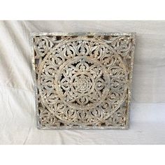 an intricately carved metal wall hanging on a white sheeted background with the image of a circular design