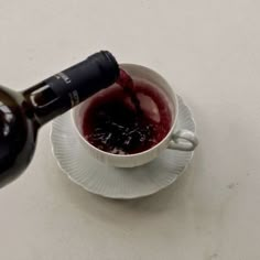 a bottle of wine is being poured into a small white cup on a saucer