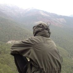 a person in a raincoat looking out over a valley and mountains from the top of a hill