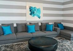 a living room with grey couches, blue pillows and a painting on the wall