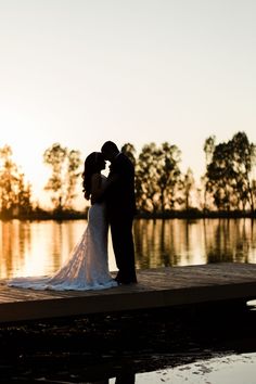 a bride and groom standing on a dock at sunset