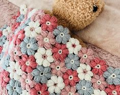 a crocheted teddy bear laying on top of a bed next to a blanket