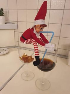 an elf sitting on top of a wine glass next to a cup filled with liquid