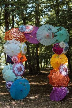 there are many different colored umbrellas hanging from the tree's branches in the forest