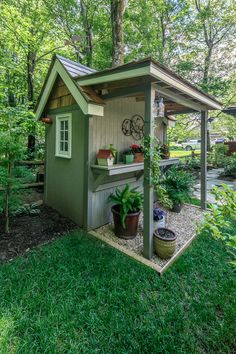 a small shed in the middle of some trees and grass with potted plants on it