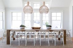 a dining room table and chairs in front of large windows with potted plants on them