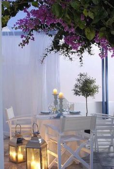 an outdoor dining area with white chairs and purple flowers on the table, lit by candles