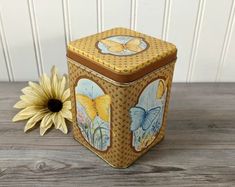 a yellow and brown box sitting on top of a wooden table next to a flower