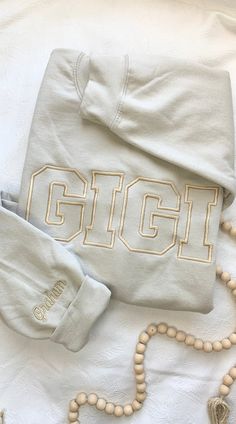 a white shirt with the word gigi on it and rosary beads laying next to it