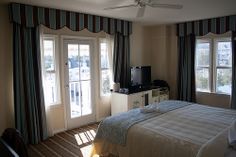 a bed sitting in a bedroom next to two windows with striped drapes on them