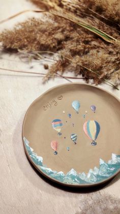 a ceramic plate with hot air balloons painted on the surface next to dry grass and dried grasses