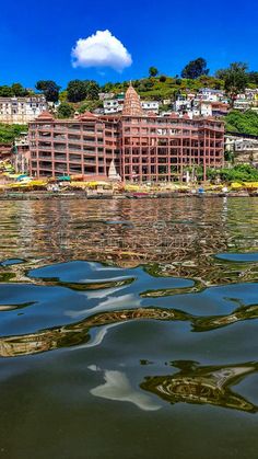 a large building sitting on top of a lake next to a lush green hillside covered in trees