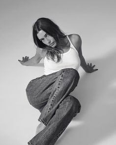 a woman in white shirt and jeans leaning on the wall with her legs spread out