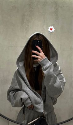 a woman taking a selfie in front of a mirror wearing a hoodie and holding a cell phone