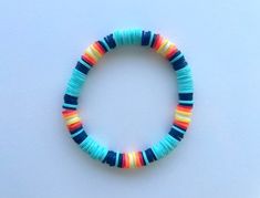 a bracelet made out of multicolored beads on a white surface with an orange, yellow, and blue bead