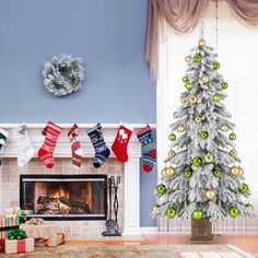 a decorated christmas tree sitting in front of a fire place with stockings hanging from it