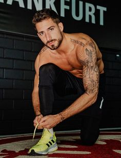 a shirtless man crouches on the floor in front of a sign