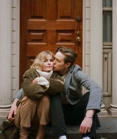 a man kissing a woman on the cheek in front of a door with autumn leaves