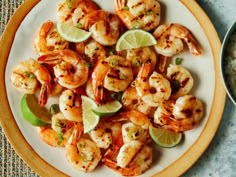 a white plate topped with shrimp and limes next to a bowl filled with rice