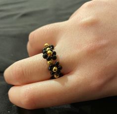 a person's hand with a ring made out of black and gold beads on it