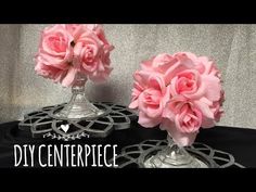 two glass vases with pink flowers in them on a black cloth covered tablecloth