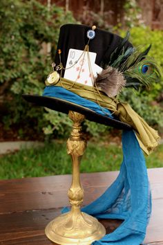 a hat with peacock feathers on it sitting on top of a wooden table next to a blue scarf