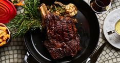 steak and fries on a pan with dipping sauces next to wine glasses, utensils and plates