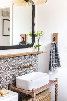 a white sink sitting under a bathroom mirror next to a wooden shelf with flowers on it