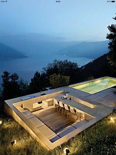 an outdoor dining area next to a swimming pool with lights on the ground and water in the background