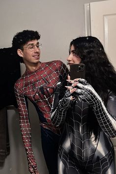 a man and woman dressed up as spider - man taking a selfie in the bathroom