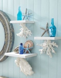 three white shelves with sea shells and blue bottles on them, against a light blue wall