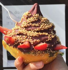 a person holding up a pastry with strawberries and chocolate frosting on it's top