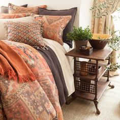 a bed with an orange and brown comforter on top of it next to a small table