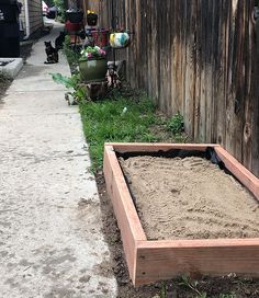 a wooden planter filled with sand next to a sidewalk and fenced in yard