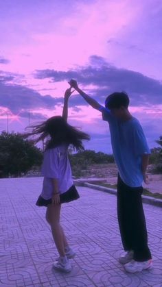 two people are dancing on the sidewalk at sunset