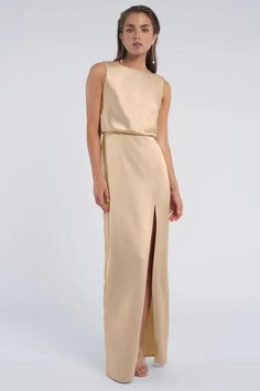 a woman wearing a beige dress with a slit down the side and an asymmetrical neckline